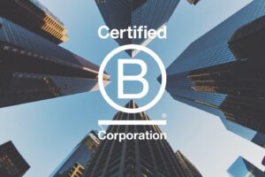 Low-angle view of skyscrapers converging towards the sky with the "certified b corporation" logo, representing sustainability, superimposed in the center.