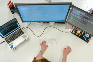 A woman sitting at a desk with two monitors and a keyboard.